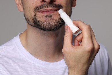 Photo of Man applying lip balm onto his lips on grey background, closeup