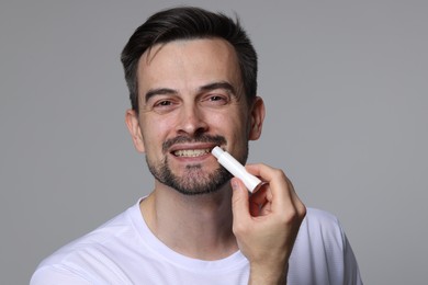 Photo of Smiling man applying lip balm onto his lips on grey background