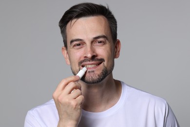 Photo of Smiling man applying lip balm onto his lips on grey background