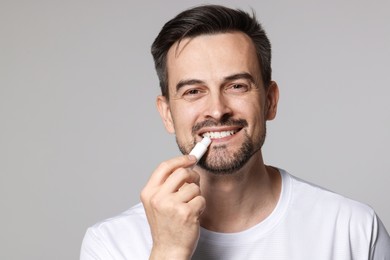 Photo of Smiling man applying lip balm onto his lips on grey background