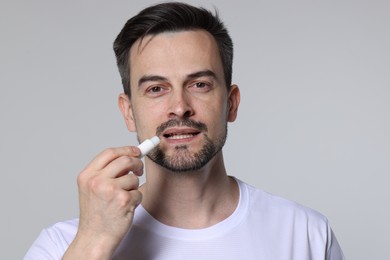 Photo of Man applying lip balm onto his lips on grey background