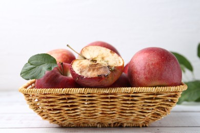 Photo of Spoiled apple and good ones in basket on white wooden table, closeup
