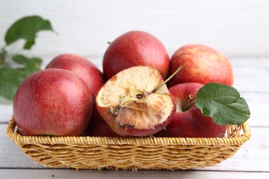 Photo of Spoiled apple and good ones in basket on white wooden table, closeup