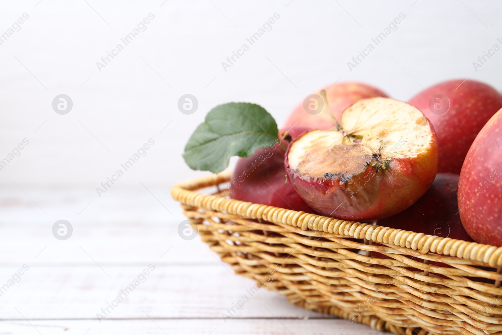 Spoiled apple and good ones in basket on white wooden table, closeup. Space for text Photo of Spoiled apple and good ones in basket on white wooden table, closeup. Space for text