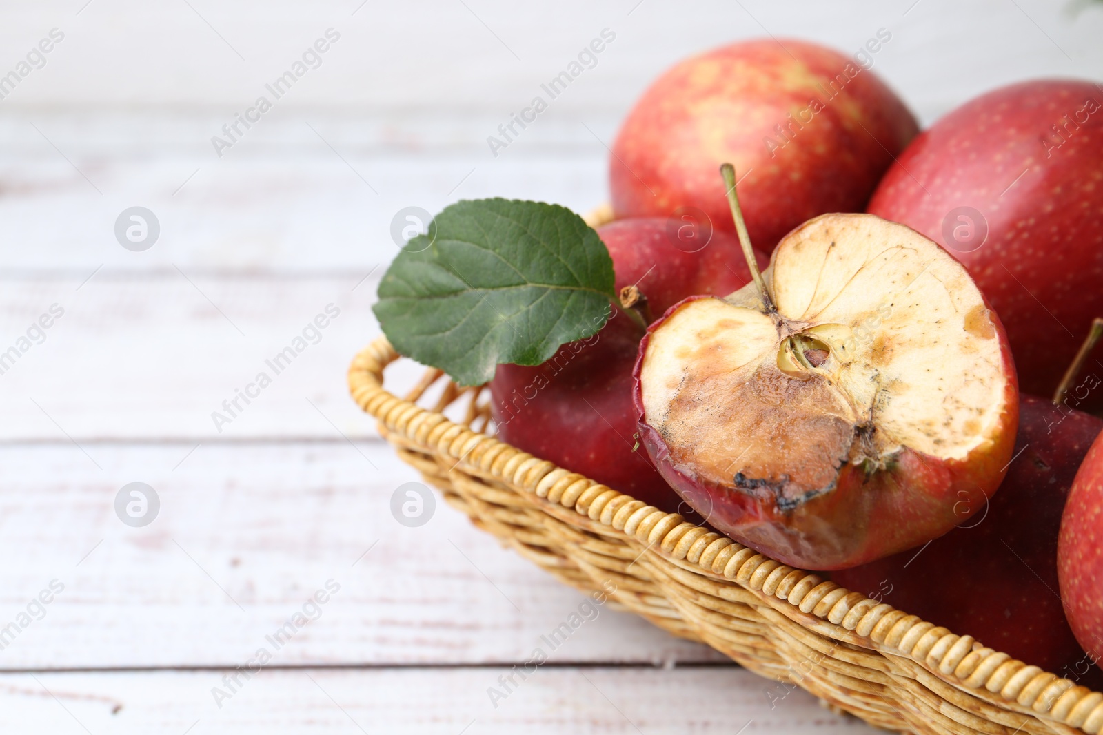 Photo of Spoiled apple and good ones in basket on white wooden table, closeup. Space for text