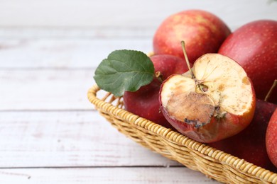 Photo of Spoiled apple and good ones in basket on white wooden table, closeup. Space for text