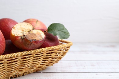 Photo of Spoiled apple and good ones in basket on white wooden table, closeup. Space for text
