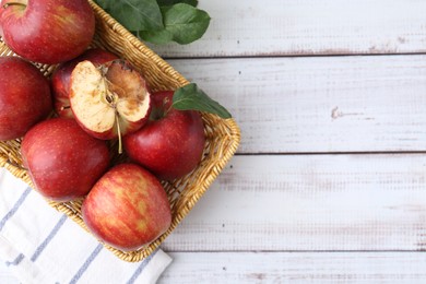 Photo of Spoiled apple and good ones in basket on white wooden table, top view. Space for text