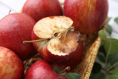 Photo of Spoiled apple and good ones in basket on table, closeup