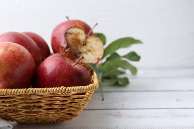 Photo of Spoiled apple and good ones in basket on white wooden table, closeup