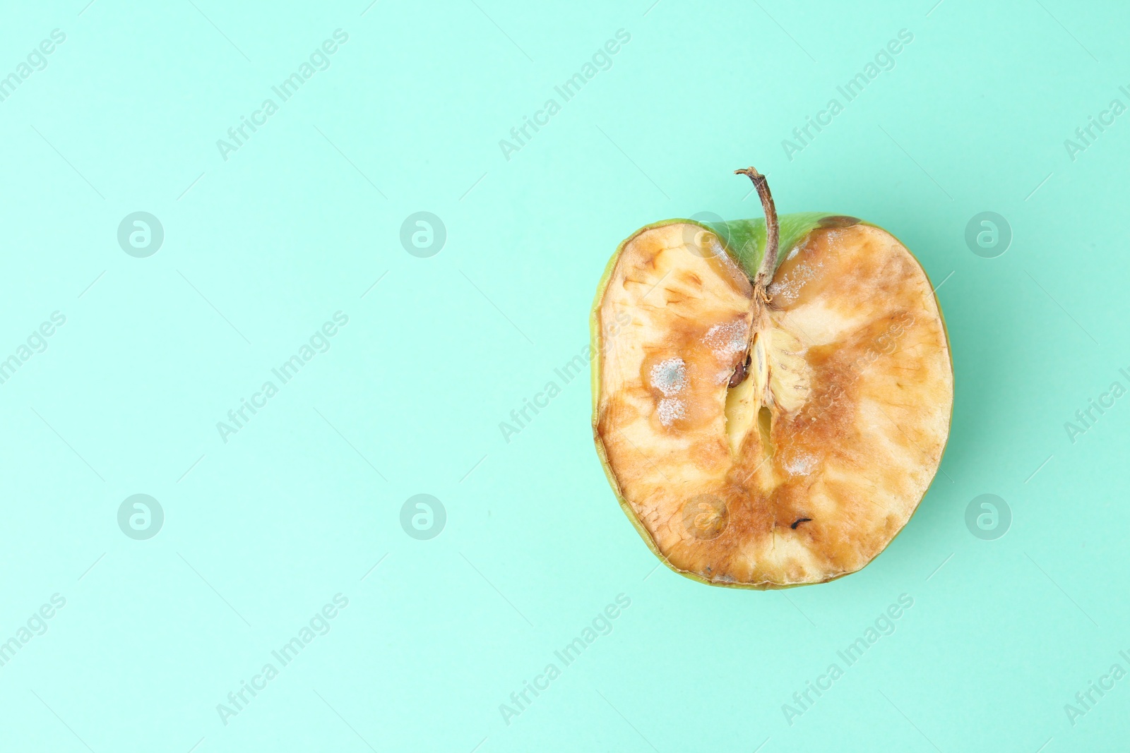 Half of spoiled apple on turquoise background, top view. Space for text Photo of Half of spoiled apple on turquoise background, top view. Space for text