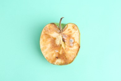 Photo of Half of spoiled apple on turquoise background, top view