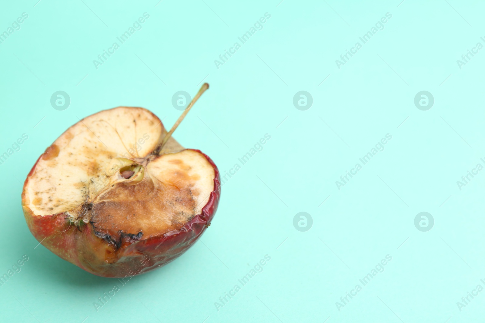 Half of spoiled apple on turquoise background. Space for text Photo of Half of spoiled apple on turquoise background. Space for text