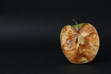 Photo of Half of spoiled apple on black background. Space for text