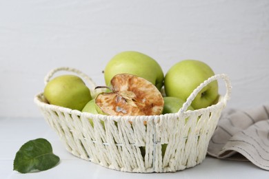 Photo of Spoiled apple and good ones in basket on white table