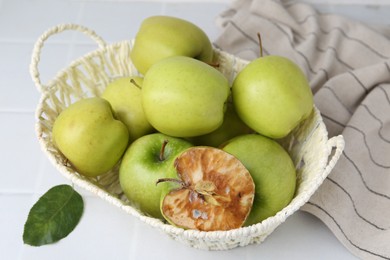Photo of Spoiled apple and good ones in basket on white table, closeup