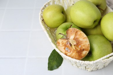 Photo of Spoiled apple and good ones in basket on white table, closeup. Space for text