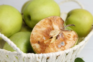Photo of Spoiled apple and good ones in basket on white table, closeup