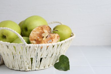 Photo of Spoiled apple and good ones in basket on white table, closeup