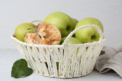 Photo of Spoiled apple and good ones in basket on white table, closeup