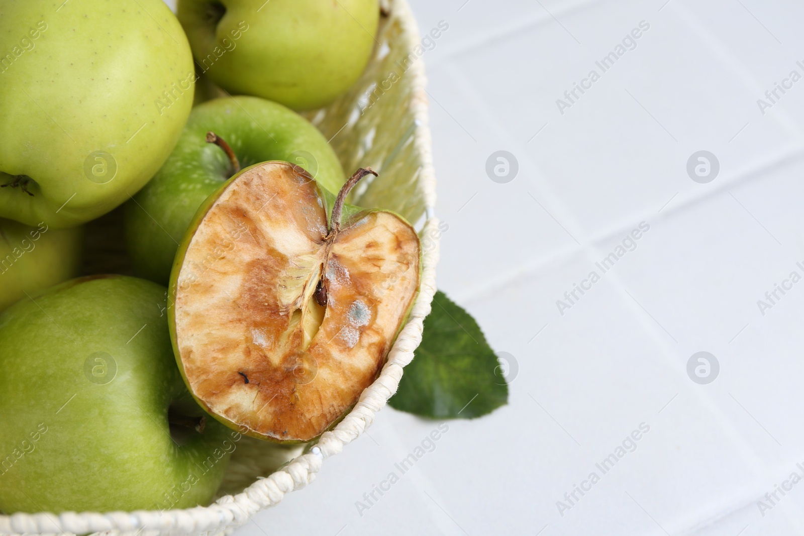 Spoiled apple and good ones in basket on white table, closeup. Space for text Photo of Spoiled apple and good ones in basket on white table, closeup. Space for text