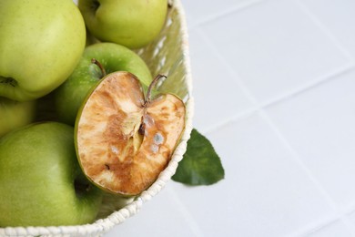 Photo of Spoiled apple and good ones in basket on white table, closeup. Space for text