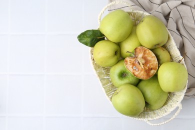 Photo of Spoiled apple and good ones in basket on white table, top view. Space for text