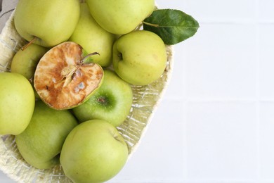 Photo of Spoiled apple and good ones in basket on white table, top view. Space for text