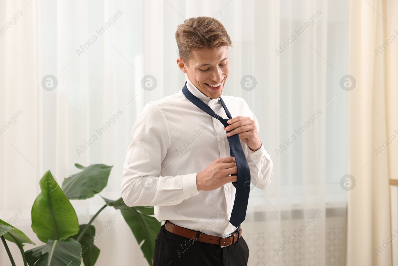 Man tying stylish blue necktie at home Photo of Man tying stylish blue necktie at home