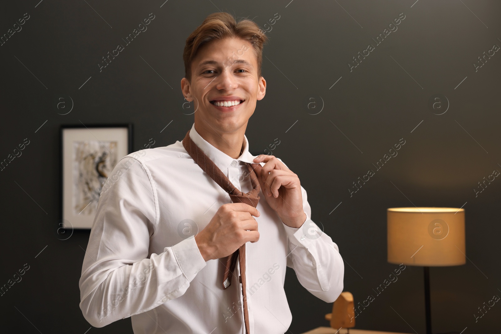 Photo of Man tying stylish brown necktie at home