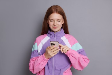 Photo of Beautiful teenage girl using smartphone on grey background