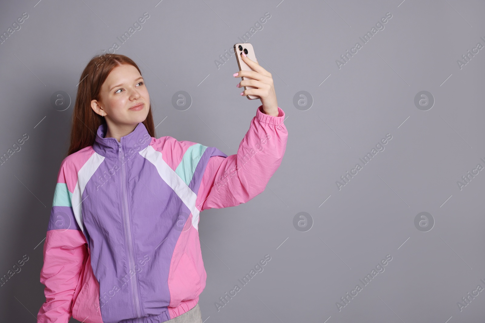 Photo of Beautiful teenage girl taking selfie by smartphone on grey background. Space for text
