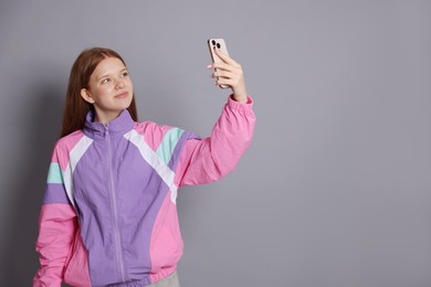 Photo of Beautiful teenage girl taking selfie by smartphone on grey background. Space for text