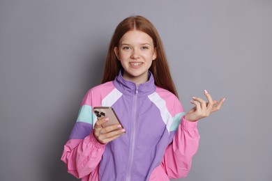 Photo of Smiling teenage girl with smartphone on grey background