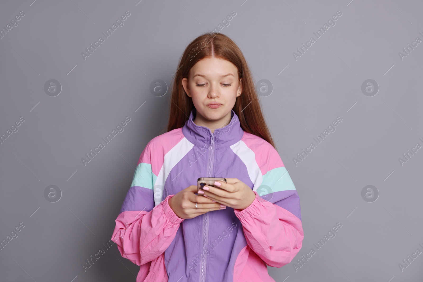 Photo of Beautiful teenage girl using smartphone on grey background