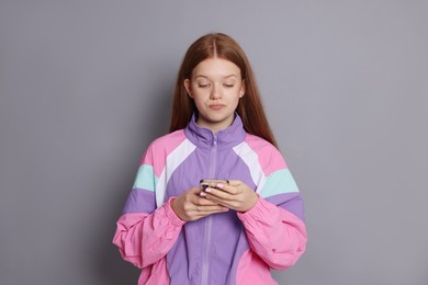 Photo of Beautiful teenage girl using smartphone on grey background