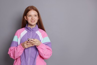 Photo of Smiling teenage girl with smartphone on grey background. Space for text