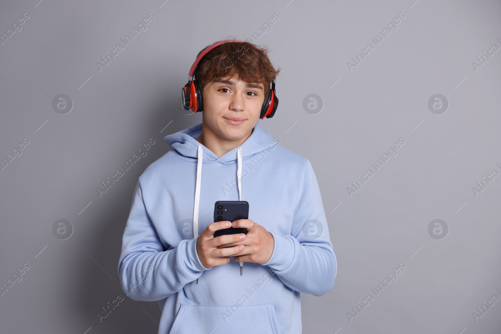 Portrait of smiling teenage boy in headphones with smartphone on grey background Photo of Portrait of smiling teenage boy in headphones with smartphone on grey background
