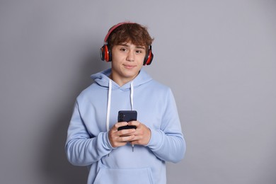 Photo of Portrait of smiling teenage boy in headphones with smartphone on grey background