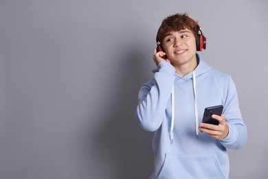 Photo of Smiling teenage boy in headphones with smartphone on grey background. Space for text
