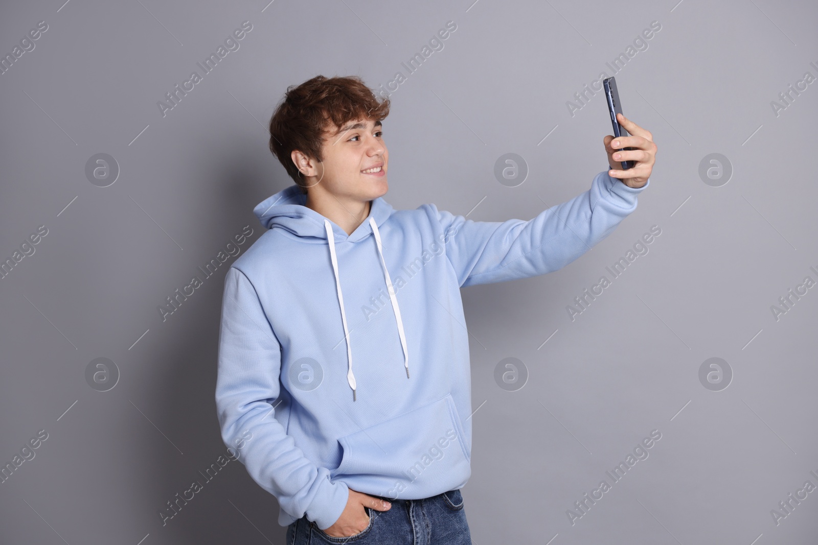 Smiling teenage boy taking selfie by smartphone on grey background Photo of Smiling teenage boy taking selfie by smartphone on grey background