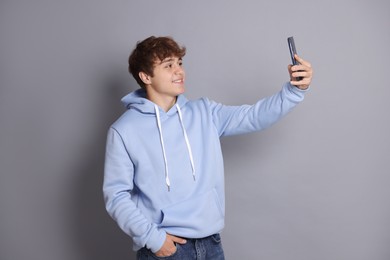 Photo of Smiling teenage boy taking selfie by smartphone on grey background