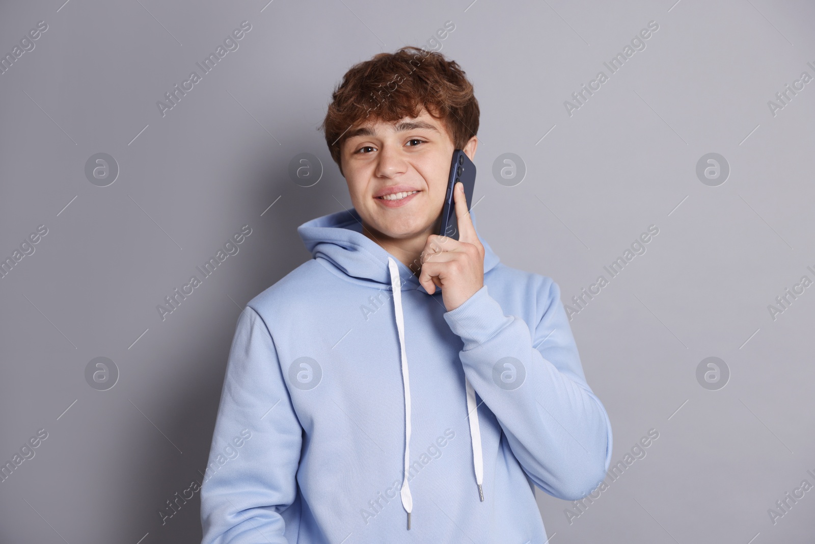 Smiling teenage boy talking by smartphone on grey background Photo of Smiling teenage boy talking by smartphone on grey background