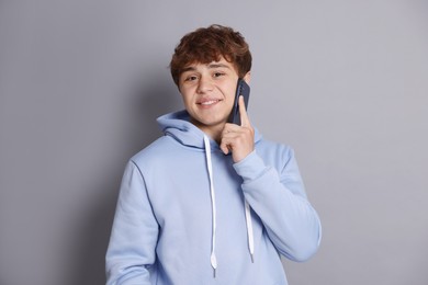 Photo of Smiling teenage boy talking by smartphone on grey background