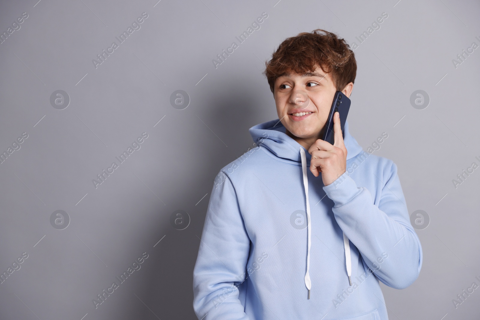 Smiling teenage boy talking by smartphone on grey background. Space for text Photo of Smiling teenage boy talking by smartphone on grey background. Space for text