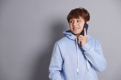 Photo of Smiling teenage boy talking by smartphone on grey background. Space for text