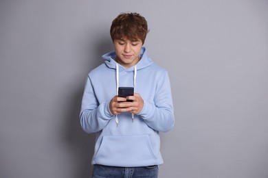 Photo of Teenage boy using smartphone on grey background