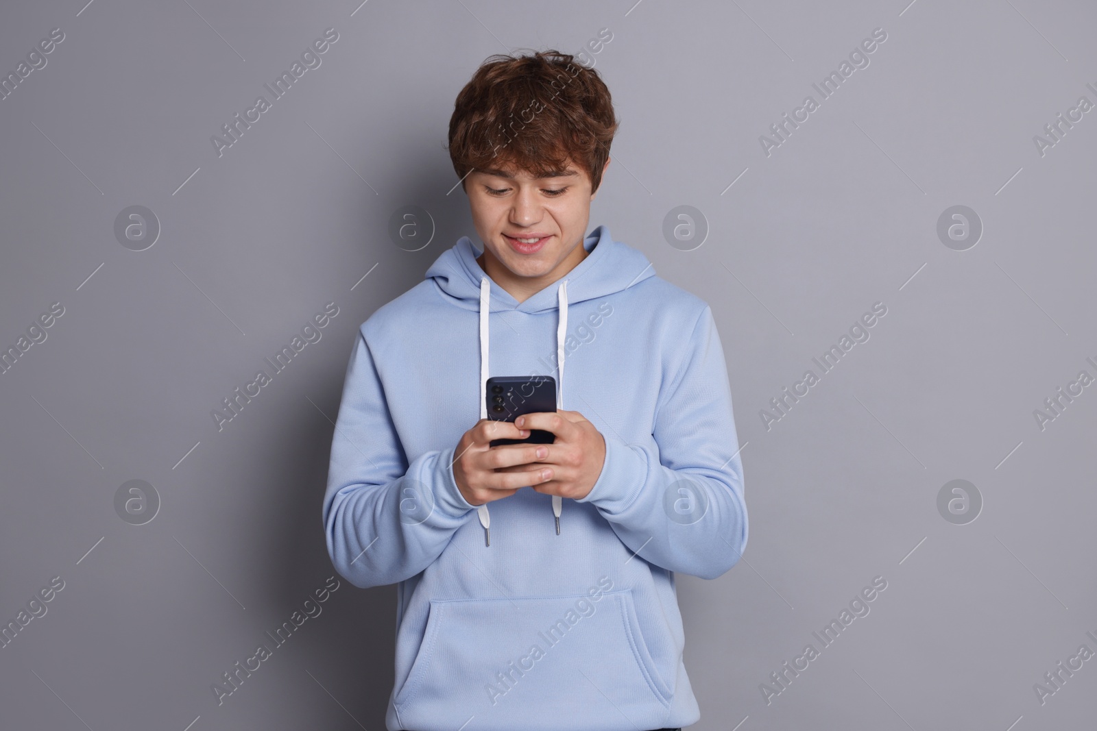 Smiling teenage boy using smartphone on grey background Photo of Smiling teenage boy using smartphone on grey background