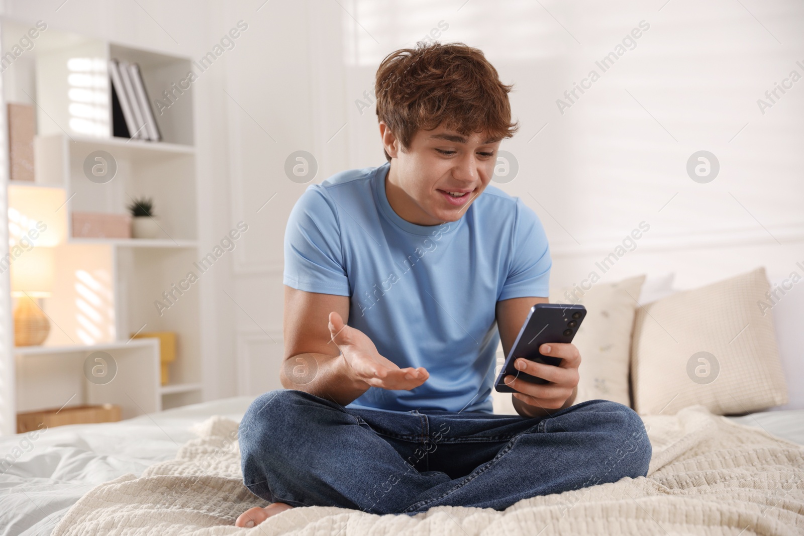 Smiling teenage boy having videocall by smartphone on bed at home Photo of Smiling teenage boy having videocall by smartphone on bed at home