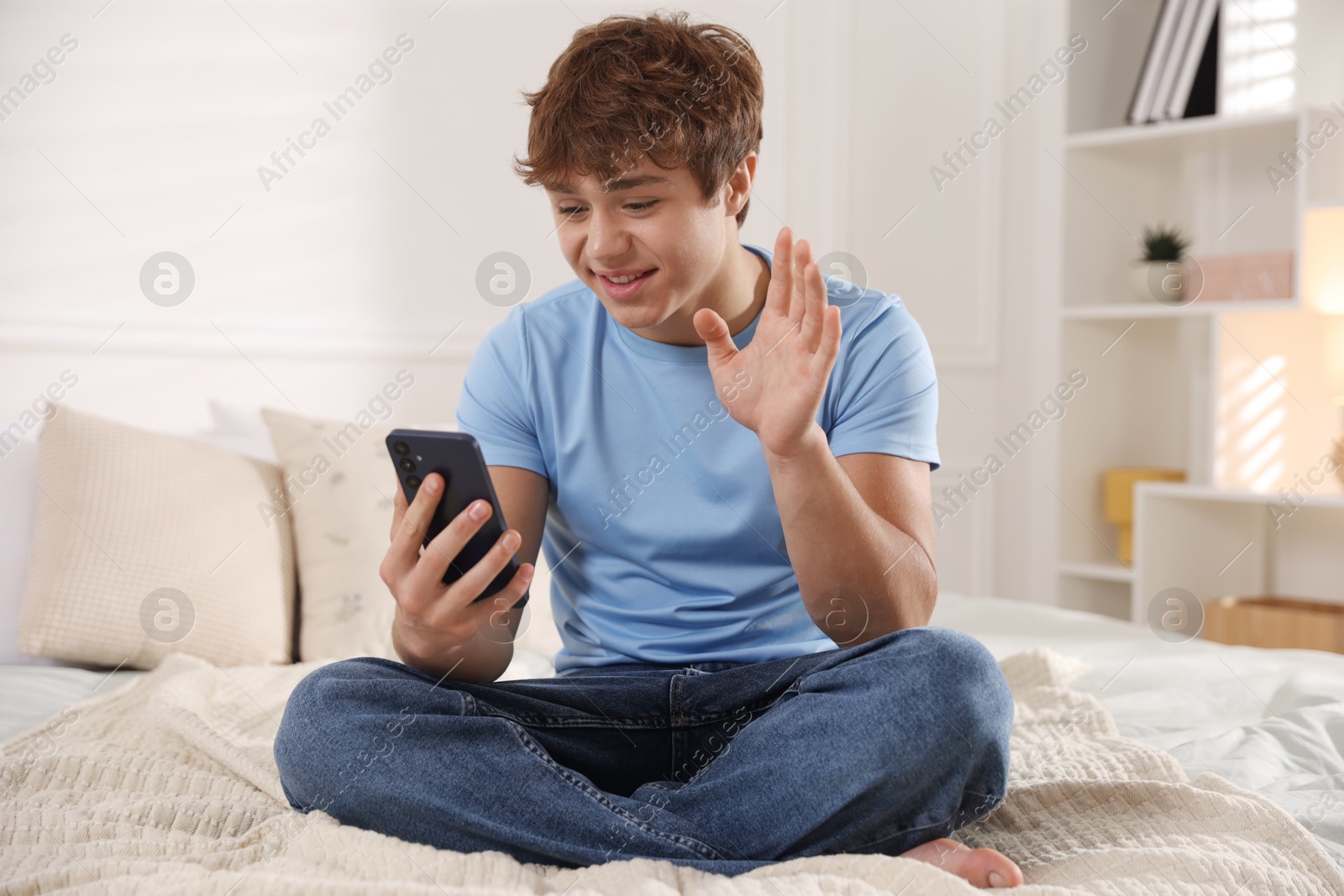 Smiling teenage boy having videocall by smartphone on bed at home Photo of Smiling teenage boy having videocall by smartphone on bed at home